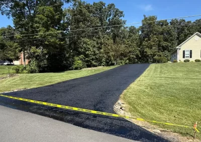Freshly paved black asphalt driveway bordered by yellow caution tape.