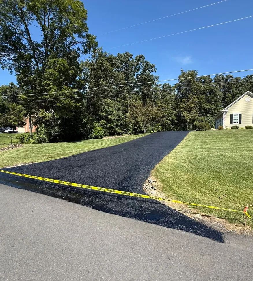 Freshly paved black asphalt driveway bordered by yellow caution tape.