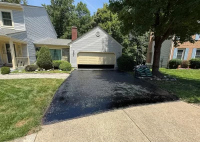 A freshly paved black asphalt driveway leading to a closed residential garage.
