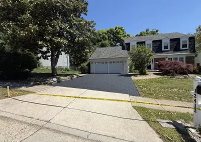 A two-story house with a newly paved asphalt driveway cordoned off by yellow caution tape.