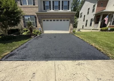 Newly paved asphalt driveway leading to a suburban house with a two-car garage.
