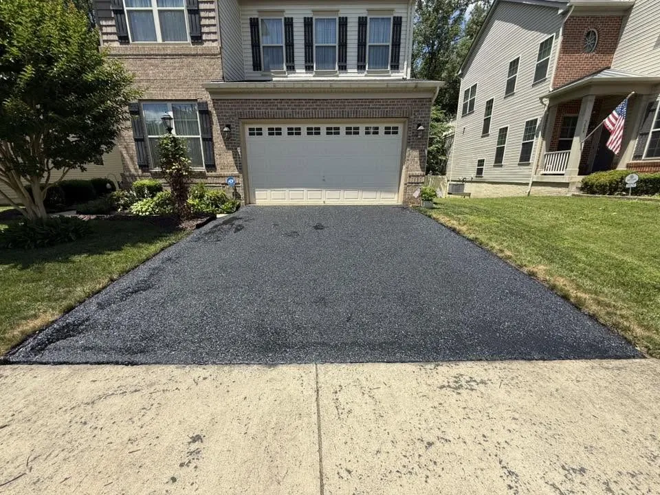 Newly paved asphalt driveway leading to a suburban house with a two-car garage.