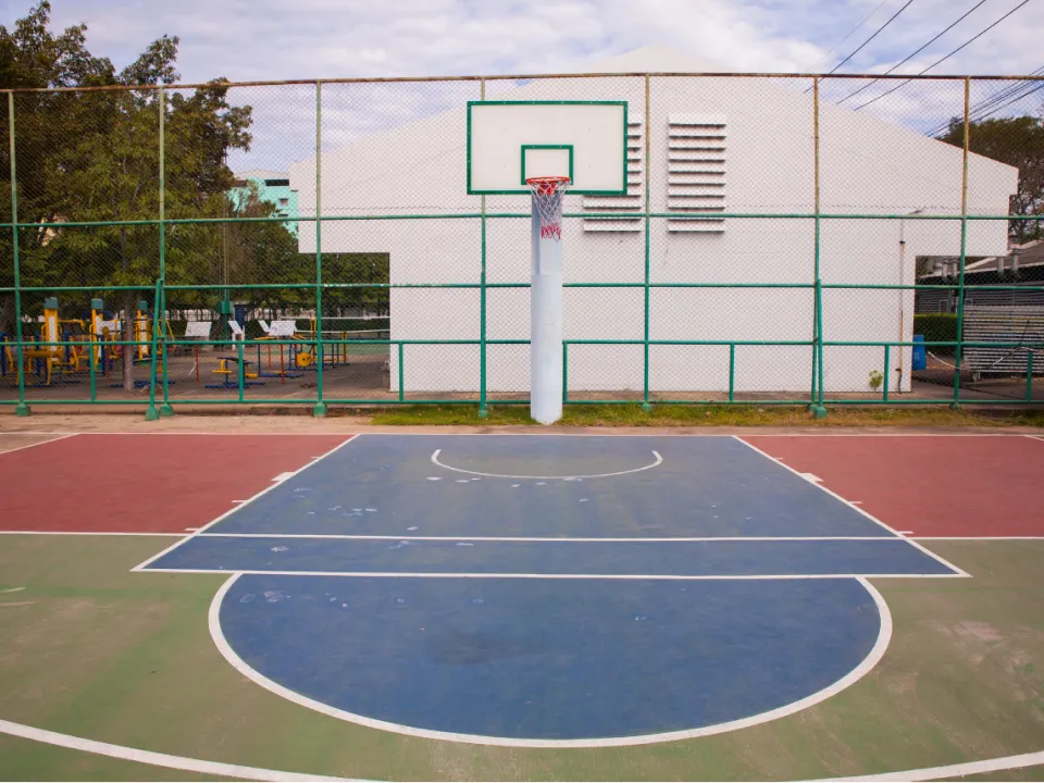 An outdoor basketball court with a blue and red playing surface enclosed by a chain-link fence.