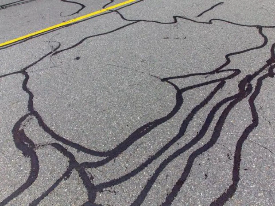 Asphalt road surface repaired with thick black crack sealant lines.
