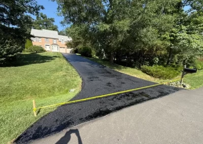 A newly paved driveway leading to a house, marked off by yellow caution tape.