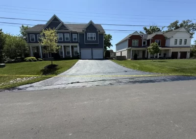 A freshly paved asphalt driveway leading to a two-story house, blocked by yellow caution tape.