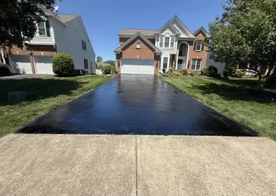 Freshly sealed black driveway leading to a two-story suburban house.