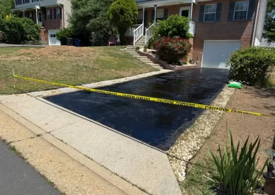 A freshly paved black asphalt driveway blocked off by yellow caution tape.
