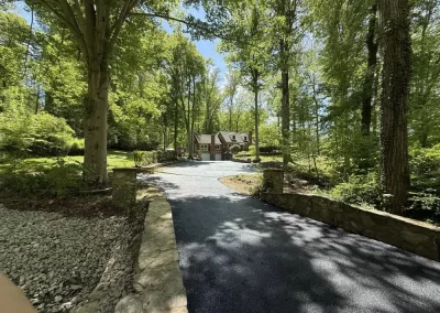 A house at the end of a long, paved driveway surrounded by trees.