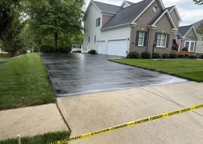 A residential driveway partially covered with fresh black asphalt and cordoned off with yellow caution tape.