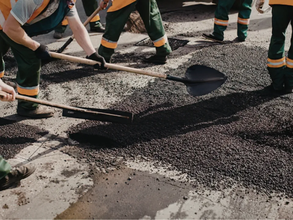Road crew workers using shovels to spread fresh asphalt on a road.