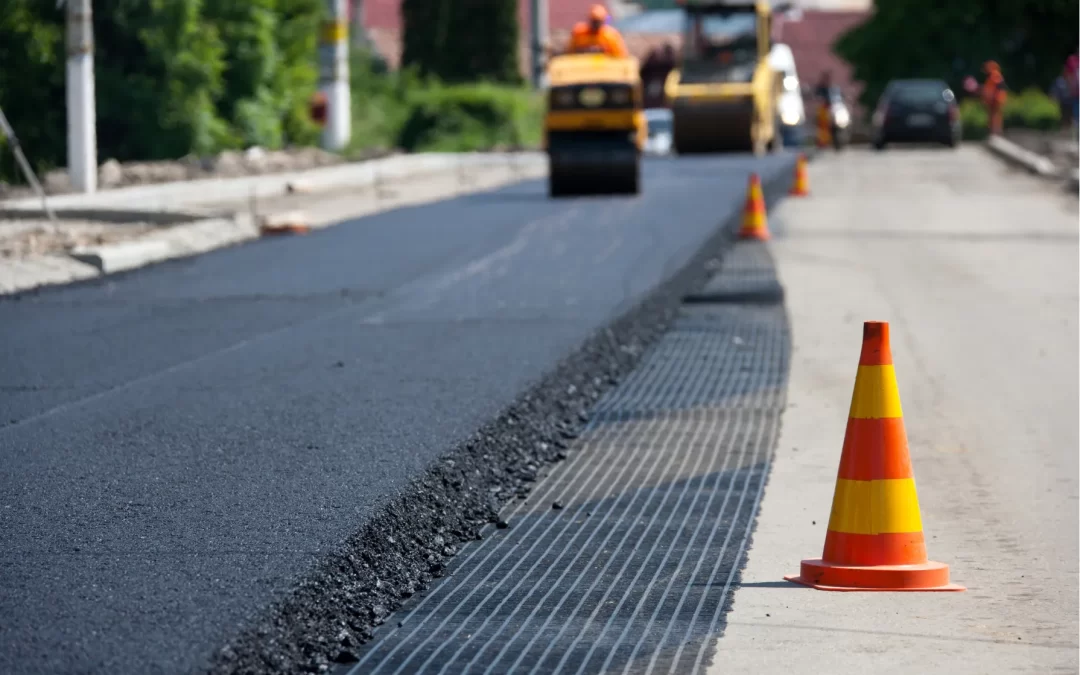 Road construction with fresh asphalt, a grid mat, and road cones.