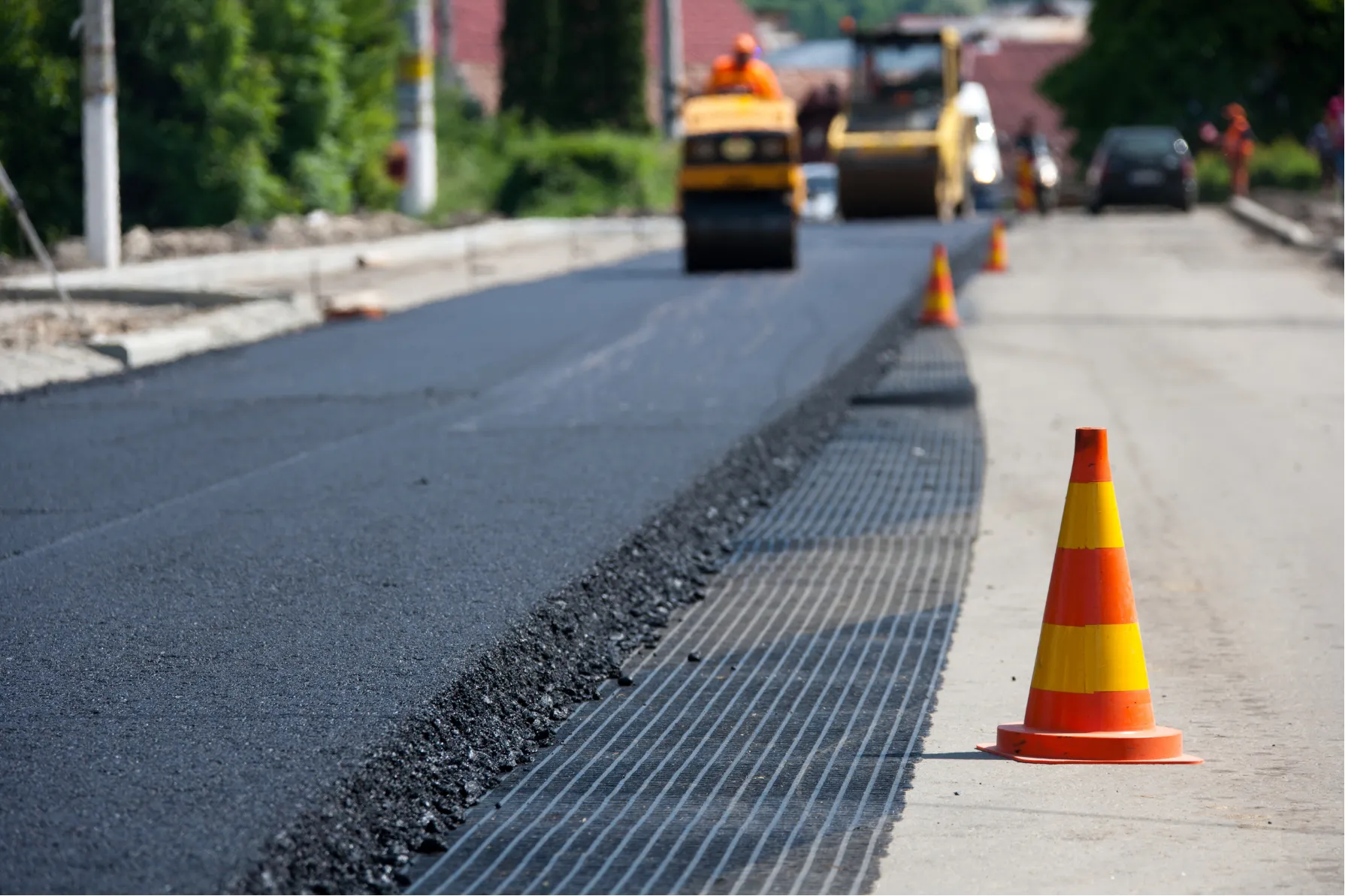 Road construction with fresh asphalt, a grid mat, and road cones.