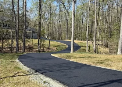 A long, winding asphalt driveway leading to a house through a wooded yard.