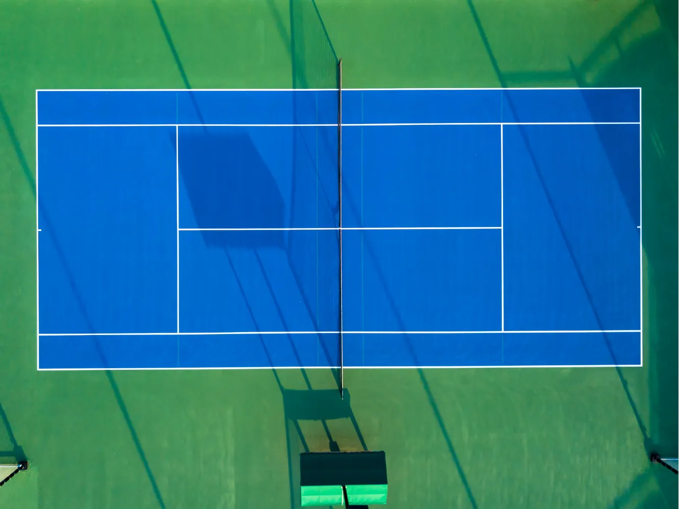 An overhead view of a blue tennis court with white lines and a net.