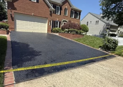 A freshly paved asphalt driveway in front of a brick house, blocked off by yellow caution tape.