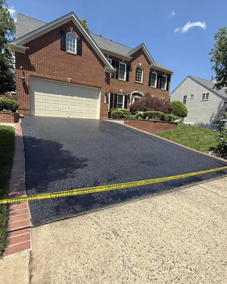 A newly paved asphalt driveway in front of a brick house, blocked off by yellow caution tape.